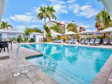 A sunny hotel pool area with palm trees, lounge chairs, and umbrellas surrounding a bright blue rectangular pool.