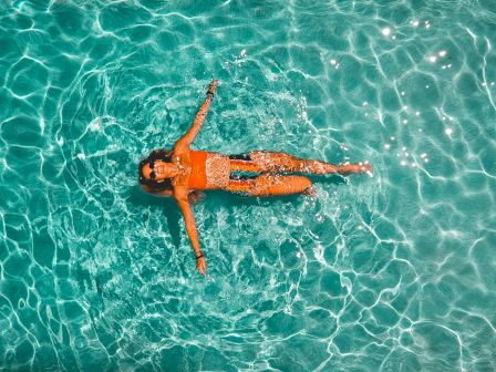 A person floating on turquoise water in a swimsuit, arms and legs relaxed, sunlit ripples surrounding them, beach vibes all around.