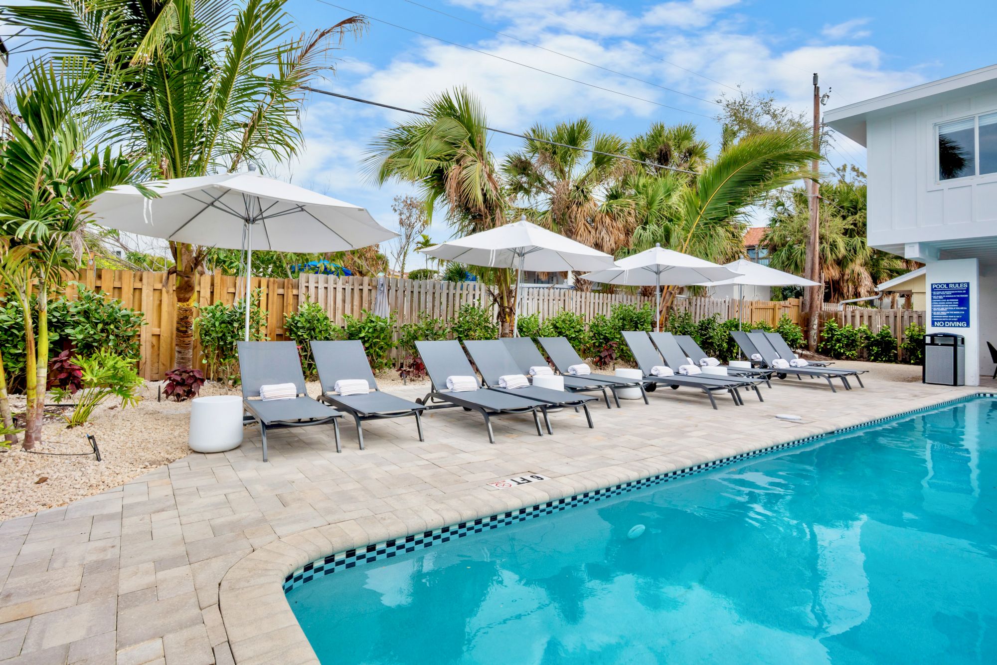 Poolside oasis with lounge chairs, umbrellas, and palm trees; a sunny courtyard vibe beside a clear blue pool, perfect for relaxation.
