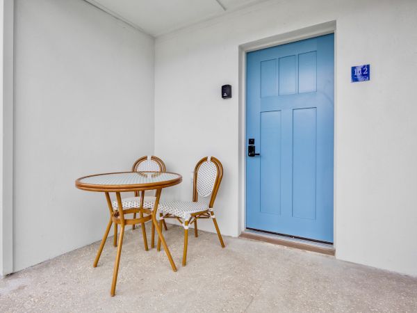 A small outdoor seating area with a round wicker table and two chairs outside a light gray wall and a bright blue door.
