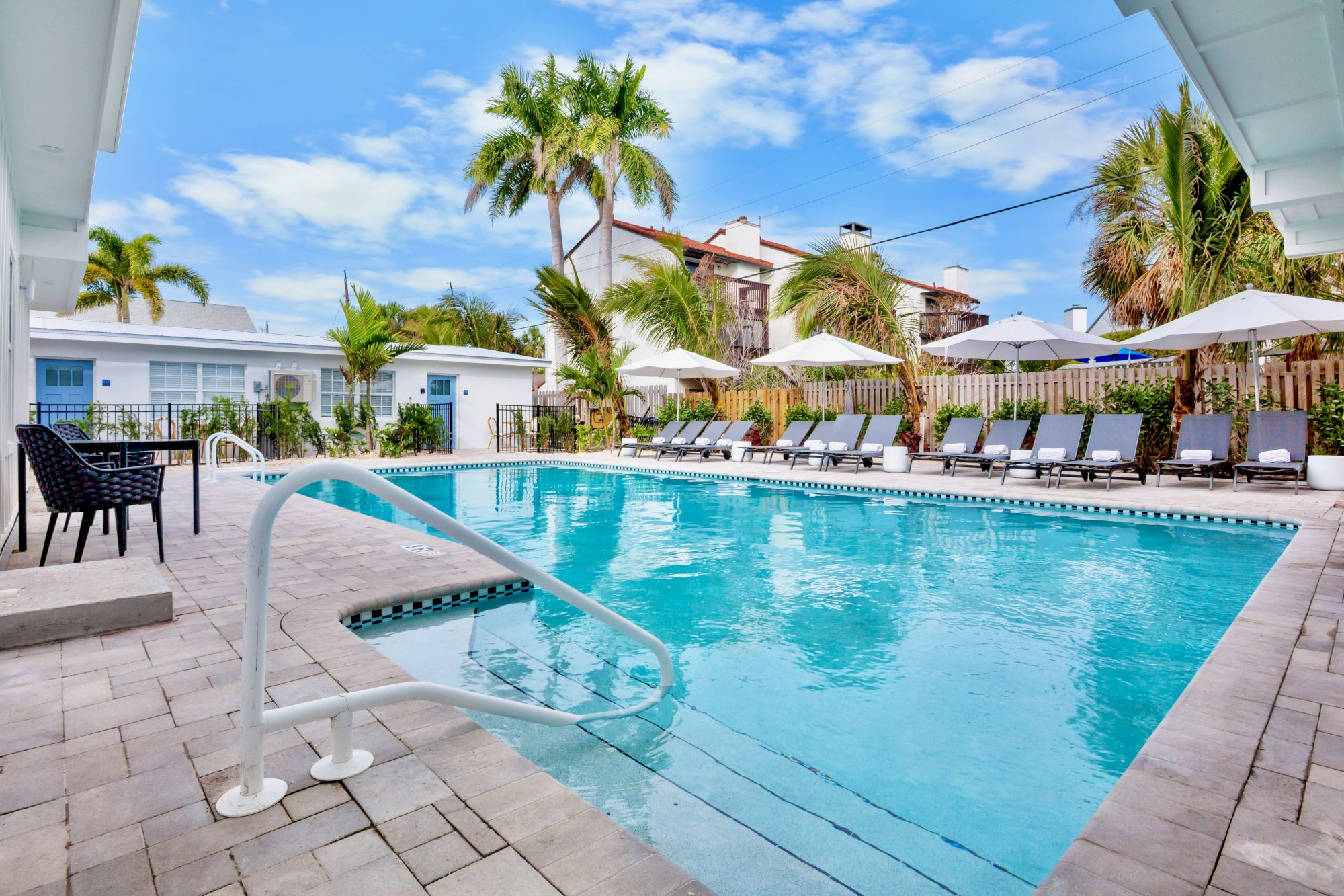 A bright resort pool area with crystal blue water, palm trees, lounge chairs, umbrellas, and a clear sky; inviting tropical vibes.