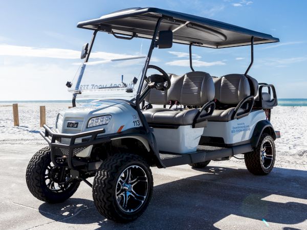 A silver beach utility golf cart with roof and seats is parked on a sunny shoreline by the ocean.